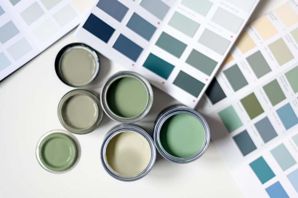 Varios botes de pintura abiertos con diferentes tonos de verde, rodeados de tarjetas de muestra de color. Centro Pinturerías