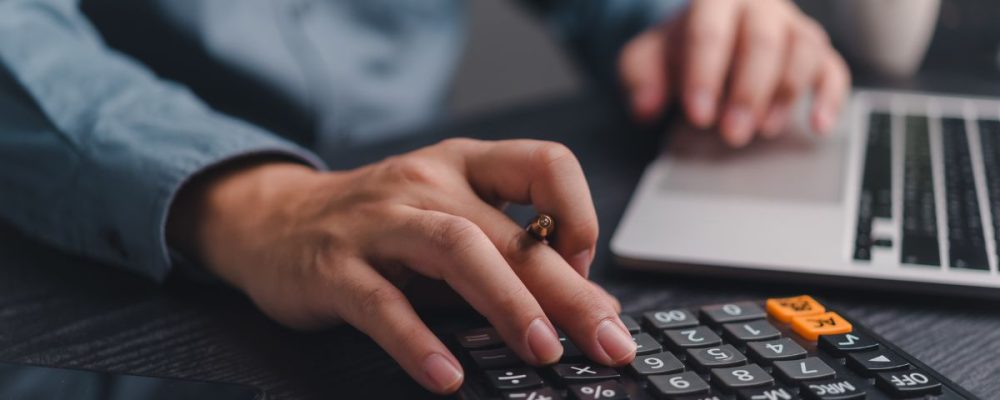 Persona usando una calculadora con una mano mientras la otra está en un teclado de laptop.